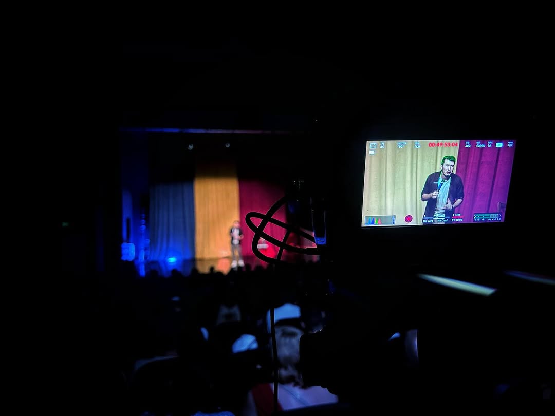 Stand-up comedy filming with cinema camera monitor showing timecode